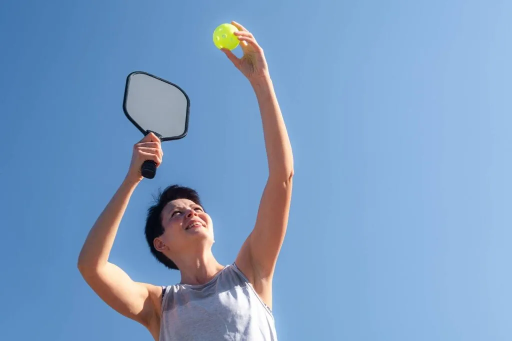 Discover the Best Pickleball Paddles for Beginners 3 Best Pickleball Paddles for Beginners: A person reaches for a yellow ball with a pickleball paddle in hand, their silhouette framed perfectly against a clear blue sky, like an exquisite header image.