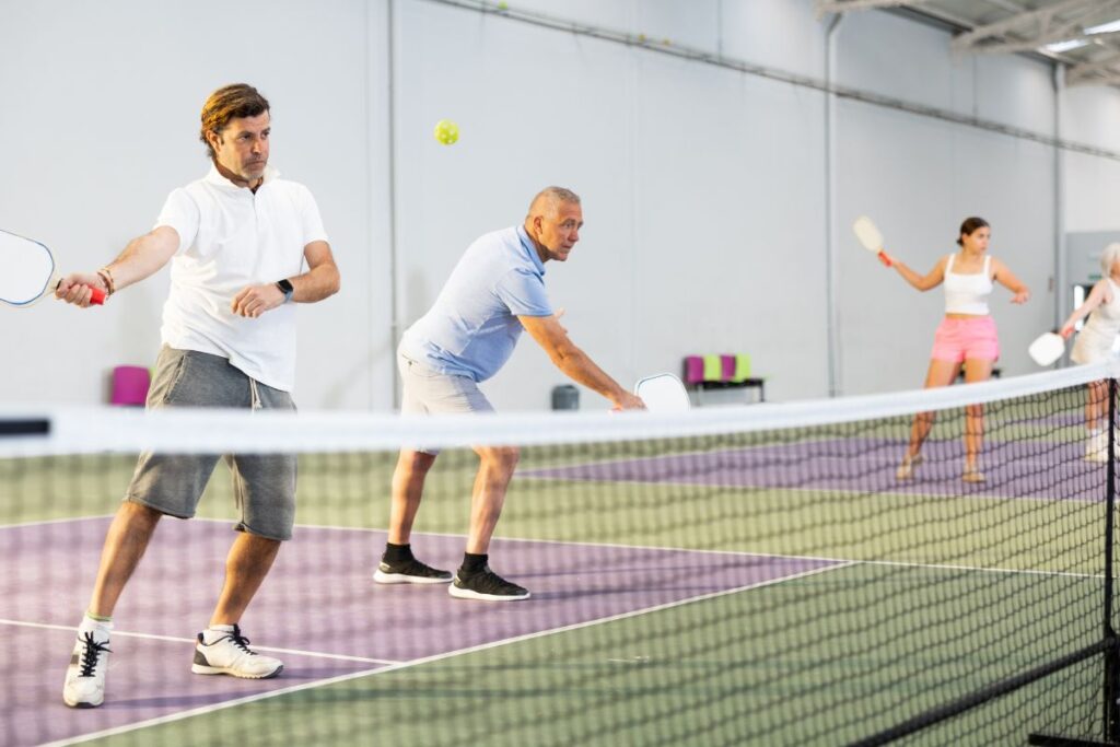 Discover the Hottest Evolving Sport: What is Pickleball 5 Four people play pickleball indoors, each intensely focused on hitting the ball with their paddles. Curious onlookers might wonder, "What is pickleball?" It's a lively game that combines elements of tennis, badminton, and ping-pong.