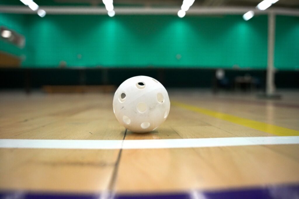 Why Pickleball Courts are the New Playground for Adults 5 Indoor pickleball courts: A white floorball lies on a wooden indoor pickleball court with green walls in the background.