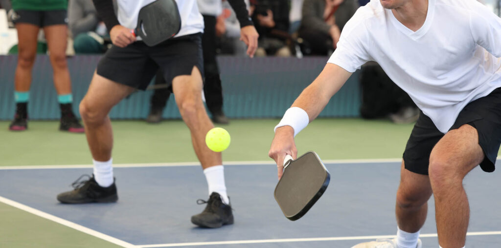 Elevate Your Game: Discover the Best Pickleball Paddles for Beginners 2 Two people in athletic gear engaged in an open play session on the pickleball court, showcasing how the best pickleball paddles for beginners can enhance control and precision while focusing intently on a yellow pickleball in mid-air.
