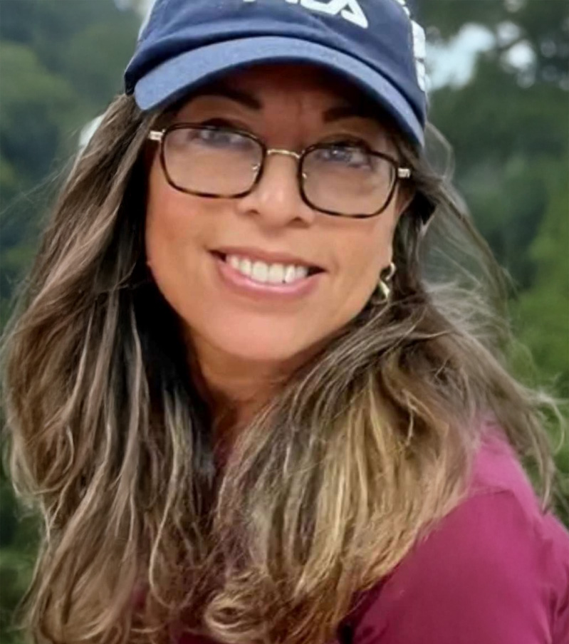Training 5 Woman with long brown hair and glasses, wearing a blue cap and maroon shirt, smiling outdoors with green trees in the background, as if featured in a dynamic content widget.