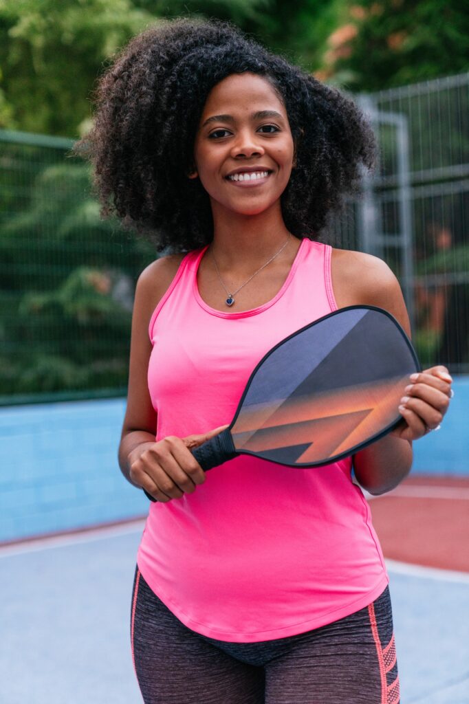 Tournaments 1 Young afro black woman holding pickleball paddle, smiling on court