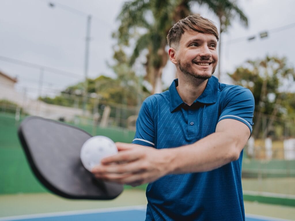 A man wearing a blue polo shirt showcases the skills of pickleball as he prepares to hit a ball with his paddle on an outdoor court.