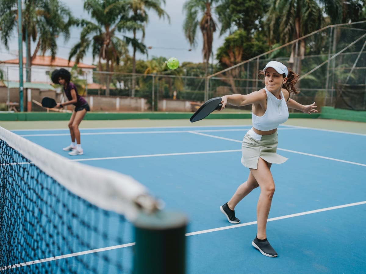 Two women compete in an exciting pickleball match on an outdoor court, with one player in the foreground hitting the ball while the other gets ready for the next move.