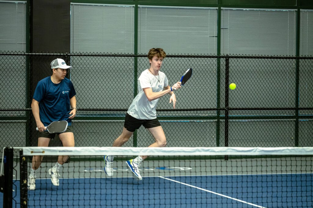 Mastering Pickleball Strategies for Beginners 10 Two people playing pickleball indoors, with one preparing to hit the ball while the other stands ready behind him—perfect for those interested in Pickleball strategies or mastering pickleball.