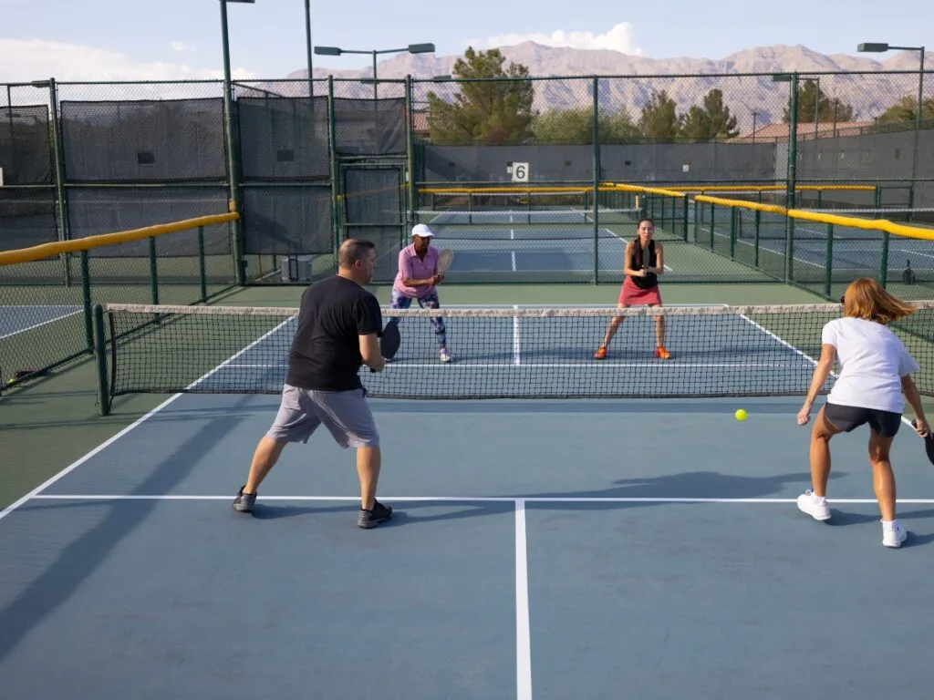 Four people are playing doubles pickleball on an outdoor court, with mountains visible in the background, carefully avoiding common pickleball faults during their match.