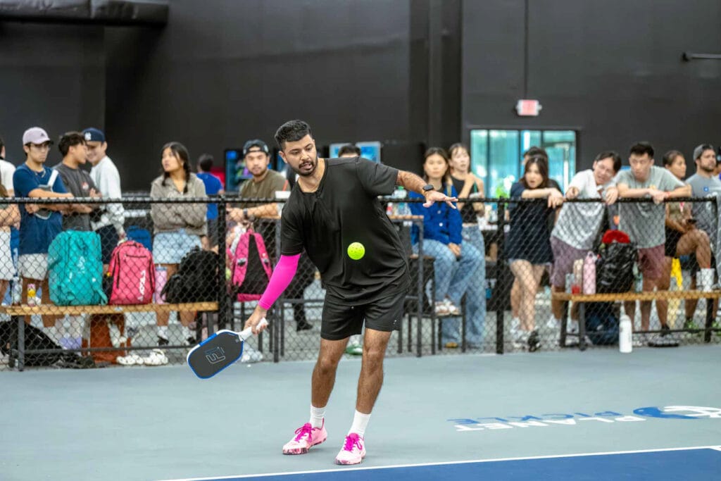 Your Essential Pickleball Pre Game Checklist 3 A man in athletic wear follows his essential pre game checklist before playing pickleball indoors, as a crowd watches from behind a fence.