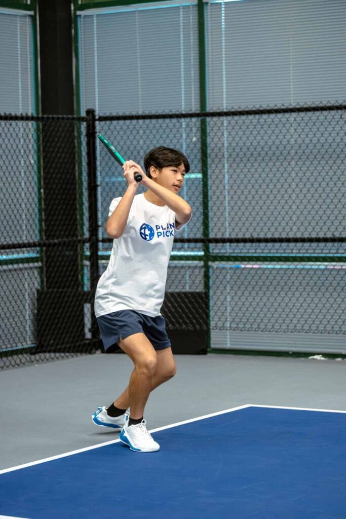 A person in athletic wear prepares to hit a pickleball with a paddle on an indoor court.