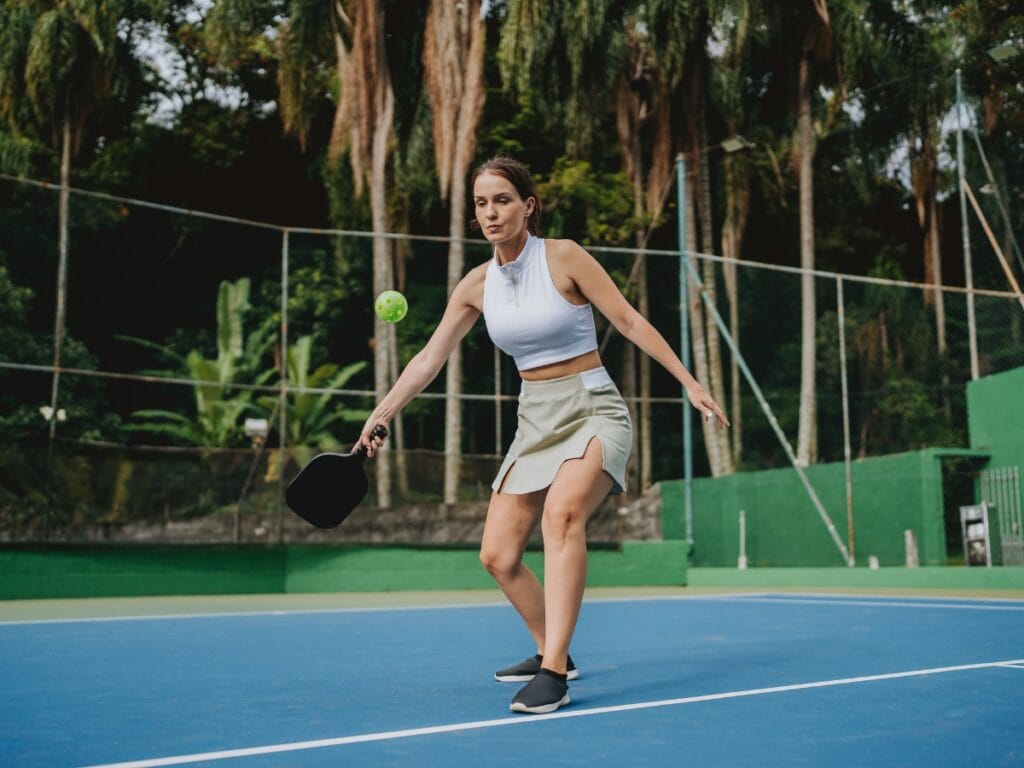 A woman in athletic attire plays pickleball on an outdoor court, focused on hitting the ball with her paddle as she follows tips from a Mastering Pickleball guide.