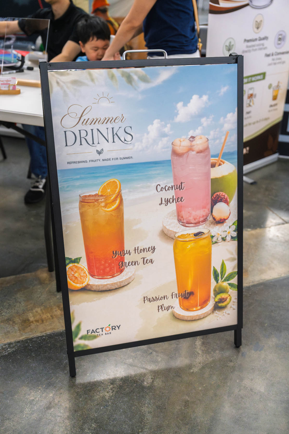 A promotional sign displays three summer drinks: Coconut Lychee, Yuzu Honey Green Tea, and Passion Fruit Plum, with images of the drinks and a beach background.