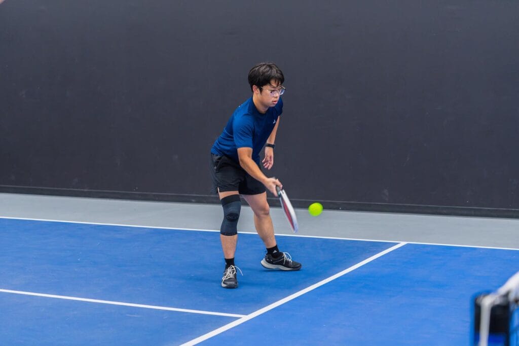 A person wearing sports attire prepares to hit a pickleball with a paddle on an indoor court.